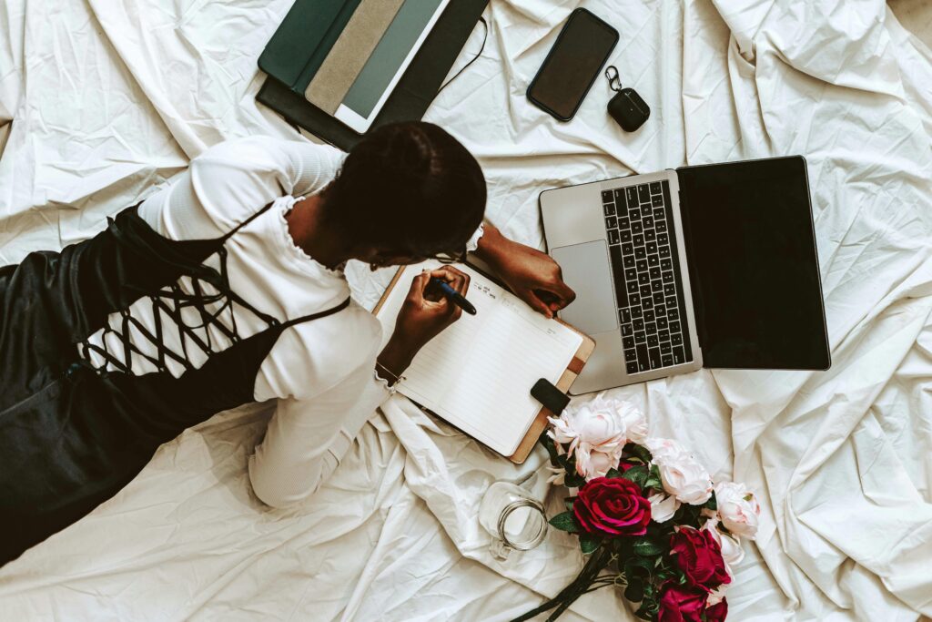 pexels-photo-17792248-17792248 African woman working remotely on laptop with notebooks and flowers around. Comfortable home setup.